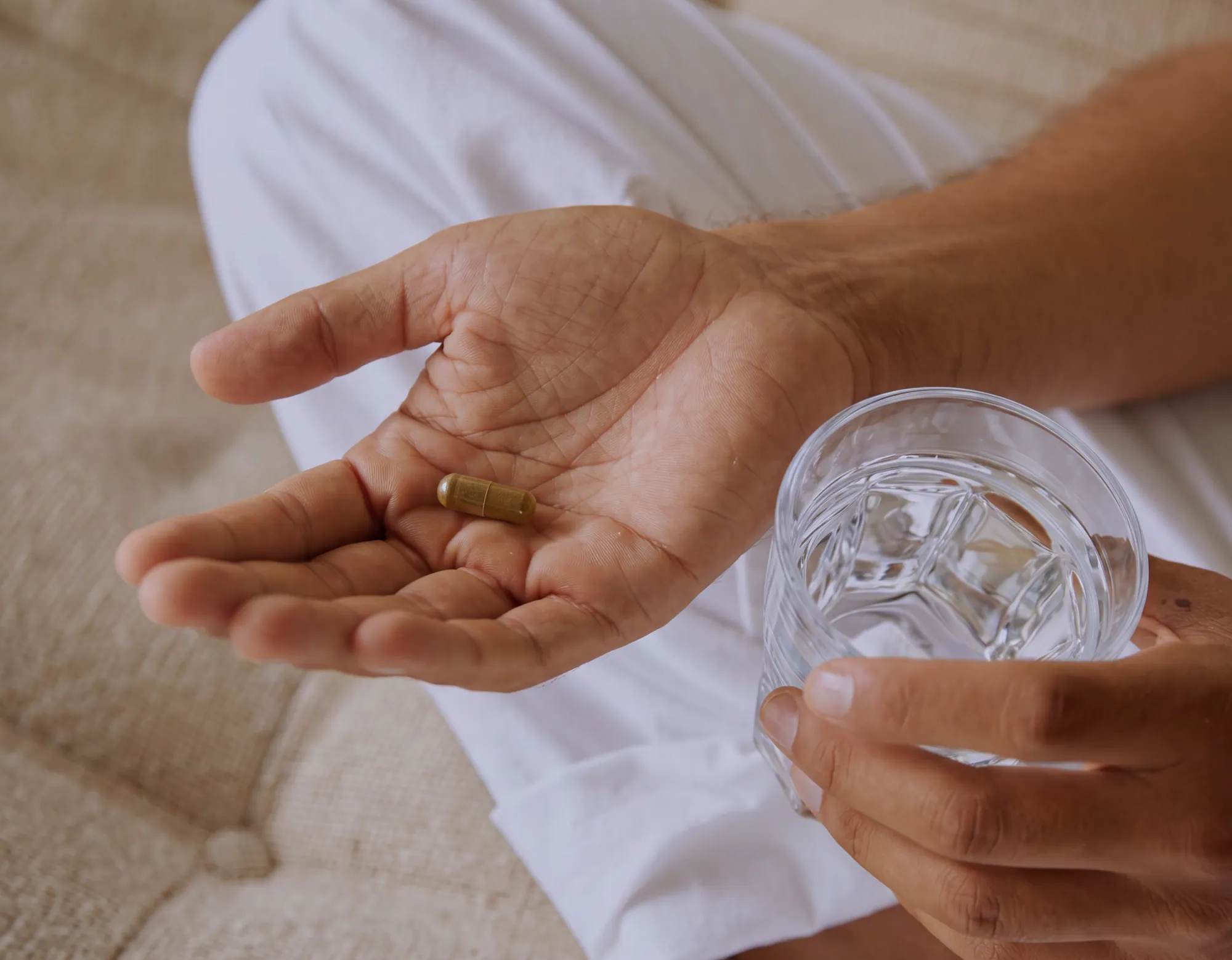 A person at home holding a capsule and a glass of water